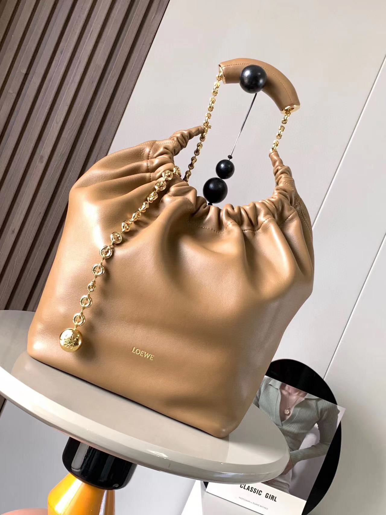 LOEWE Small Squeeze Bag: Where Elegance Meets Innovation in Luxurious Nappa Leather. The Squeeze bag embodies sophistication and femininity, crafted from luxurious nappa leather. It stands as a masterpiece, seamlessly blending traditional craftsmanship, innovative research, and distinctive design elements. The bag features a surprisingly lightweight ruched body, complemented by an adjustable donut chain and a tactile, squeezable handle. This particular version showcases the elegance of nappa lambskin in a compact size, adding an extra touch of refinement to its allure.