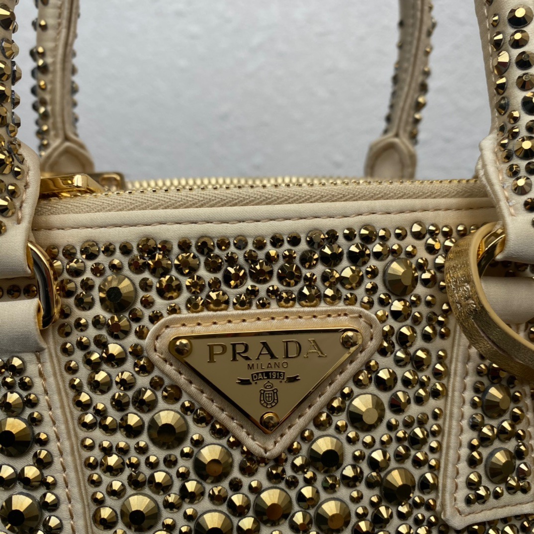 PRADA Galleria Satin Mini Bag With Crystals. Original Quality Bag including gift box, care book, dust bag, authenticity card. A surface of dazzling crystals in various sizes creates a precious play of sparkles and glimmers on this Prada Galleria bag, recalling the jewelry world. The accessory, which exemplifies the centennial excellence of Prada in luxury leather goods, becomes a reflection of the brand's modernity and stylistic identity that seeks to interpret kaleidoscopic contemporaneity through a pragmatic design and structured lines. Presented in a mini version, the bag is made of fine silk satin. The Prada Galleria bag, named after the historic Prada store opened by Mario Prada in 1913 in Galleria Vittorio Emanuele II in Milan, expresses the quintessence of the brand's timeless elegance.