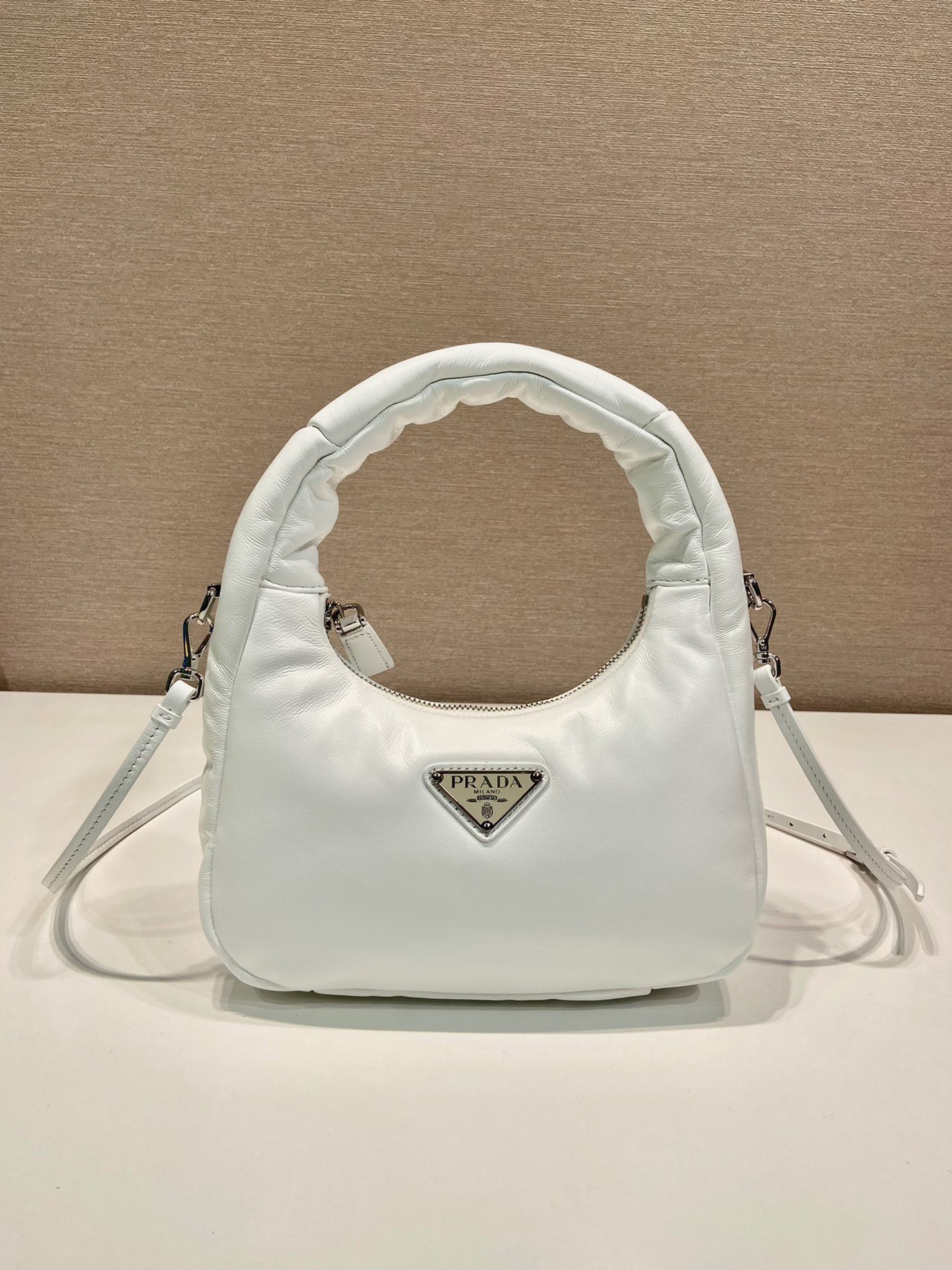 PRADA Soft Padded Mini Bag. Original Quality Bag including gift box, care book, dust bag, authenticity card. A harmonious, bold silhouette characterizes this mini-bag made of padded leather accented with the detachable, adjustable shoulder strap. Defined by its versatile allure, the accessory has a zipper closure and is decorated with the emblematic enameled metal triangle logo.