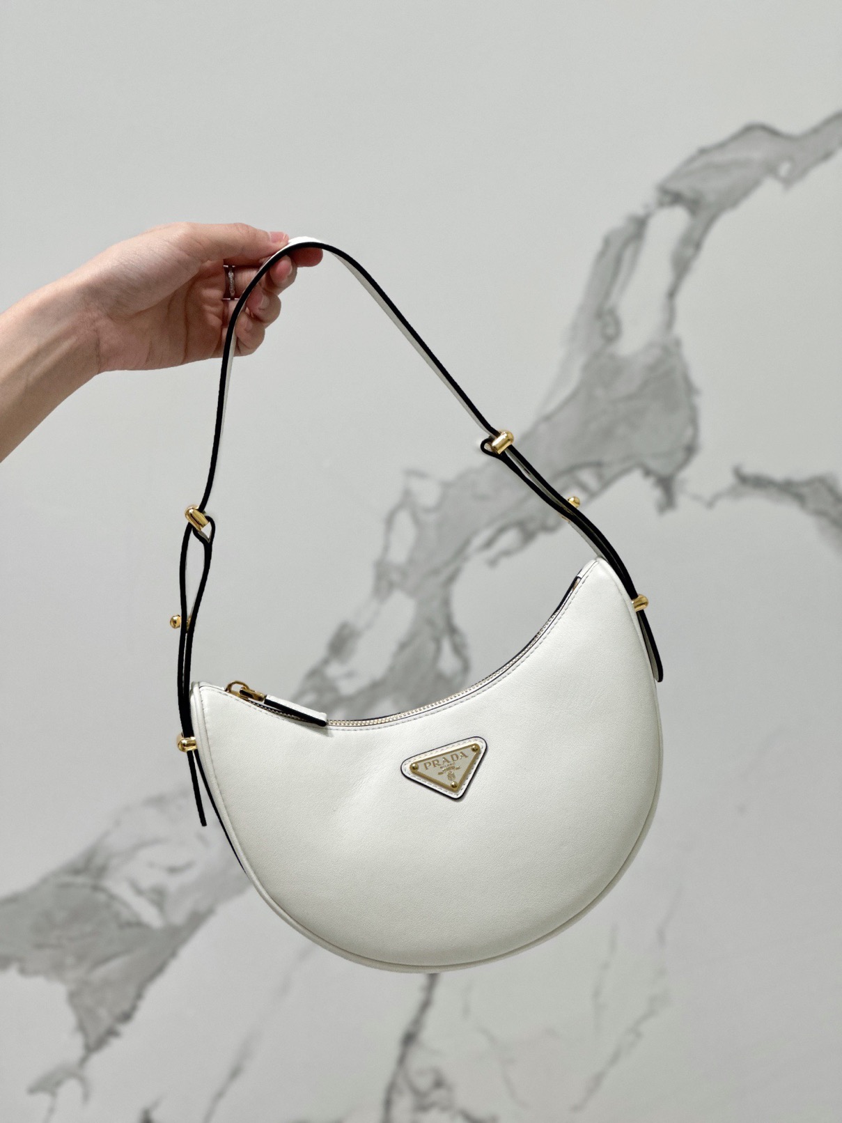 PRADA Leather Shoulder Bag. High-End Quality Bag including gift box, care book, dust bag, authenticity card. This sleek leather bag expresses versatile, modernist allure. The accessory with a curvy silhouette is completed by the leather extension for versatile wear. With a nappa leather lining and metal hardware, the bag is accented with the iconic enameled metal triangle logo on the front.