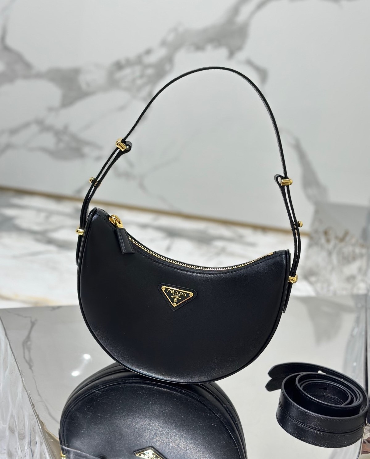 PRADA Leather Shoulder Bag. High-End Quality Bag including gift box, care book, dust bag, authenticity card. This sleek leather bag expresses versatile, modernist allure. The accessory with a curvy silhouette is completed by the leather extension for versatile wear. With a nappa leather lining and metal hardware, the bag is accented with the iconic enameled metal triangle logo on the front.