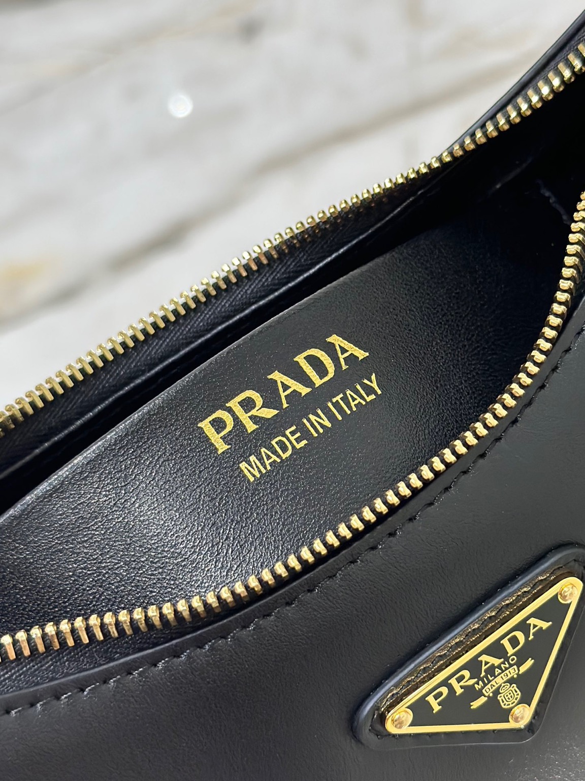 PRADA Leather Shoulder Bag. High-End Quality Bag including gift box, care book, dust bag, authenticity card. This sleek leather bag expresses versatile, modernist allure. The accessory with a curvy silhouette is completed by the leather extension for versatile wear. With a nappa leather lining and metal hardware, the bag is accented with the iconic enameled metal triangle logo on the front.