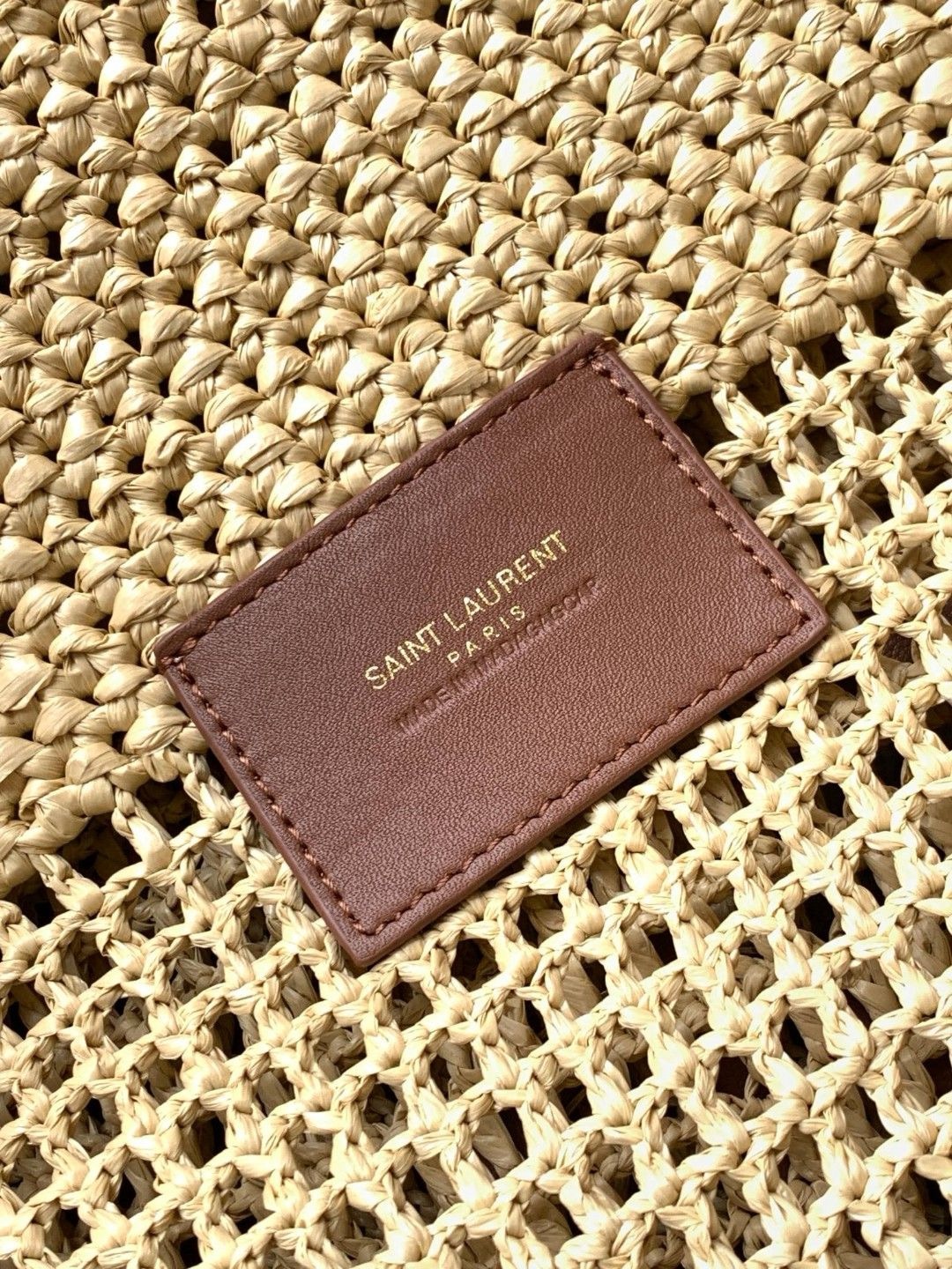 SAINT LAURENT ICare In Raffia: Handcrafted Elegance with Versatile Style. Introducing the Maxi Shopping Bag, exquisitely crafted from hand-embroidered natural raffia. This exceptional piece showcases the finest savoir-faire and specialized craftsmanship. Adorned with an oversized, sculptural Cassandre, the bag features an inner chain that can be used to adjust the sides for versatile styling. Additionally, it comes with a removable raffia sunglasses case, elegantly attached by a long chain, blending functionality with high fashion.