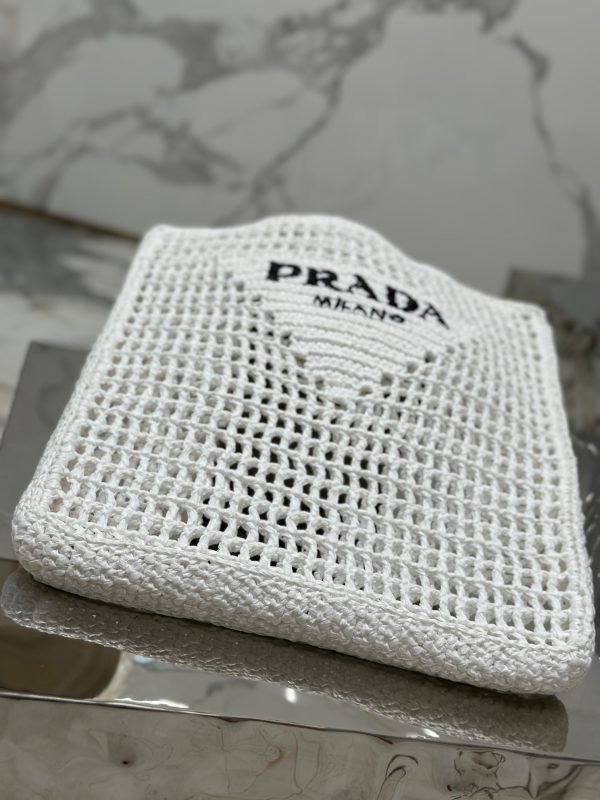 PRADA Crochet Tote Bag. Elevate your style with Prada's signature tote bag. This tote bag is the perfect addition to any summer wardrobe! Adorned with Prada's iconic triangle logo and embroidered lettering, its soft, deconstructed design is made with a light and natural raffia-effect yarn. It's sure to add an elevated touch to your ensemble.