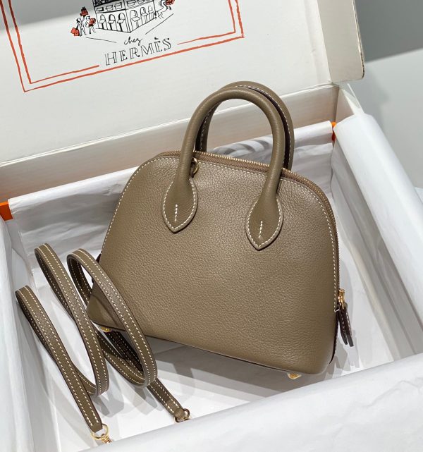 HERMÈS Bolide 1923 Mini. Timeless Elegance, Unparalleled Convenience: The Bolide Bag – A Journey in Every Stitch. Created in 1923 with the discerning needs of elite drivers and seasoned long-distance travelers in mind, this globe-trotting bag effortlessly finds its place within any automobile trunk. Its iconic round-angled shape owes its origins to the zip fastener, a novel invention introduced to France by Émile Hermès in the late 1910s, and this innovative feature enables swift access to its contents. The Bolide bag is available in various sizes, including a travel-sized version, and a range of handbag options, offering both style and functionality to its fortunate owners.