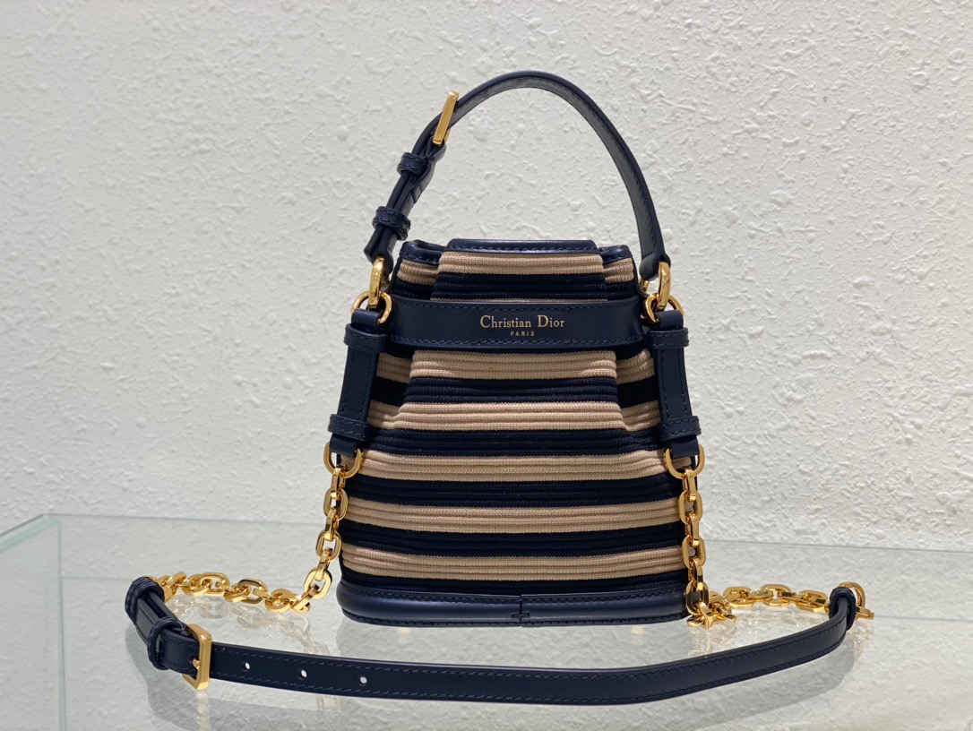 DIOR Small C'est Bag: Timeless Elegance, Effortless Style. Introducing the C'est Dior bag, a timeless and elegant creation for Fall 2023. Crafted in natural and denim blue raffia, it beautifully features the classic Marinière motif from ready-to-wear. Securing your essentials with a sophisticated CD Lock closure adorned with a twisting letter D, this bucket bag combines style with practicality. With a top handle and an adjustable, removable chain strap featuring a leather insert, this small-sized bag offers versatile carrying options—be it hand-held or comfortably draped over the shoulder.