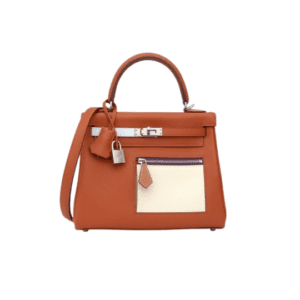 Brown leather handbag with top handle, front zip pocket, and a beige front patch pocket accented by a small luggage tag and lock accessory.